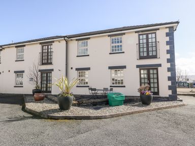 An exterior view of a two-story building with multiple windows and doors a seating area and potted plants outside at Harbour View in Porthmadog