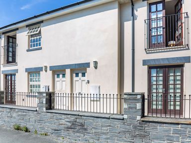 Exterior view of a building with stone wall black metal railing white doors and windows at Harbour View in Porthmadog