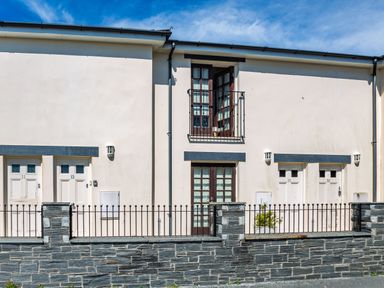 Exterior of a building with multiple white doors and windows behind a stone wall and metal fence at Harbour View in Porthmadog