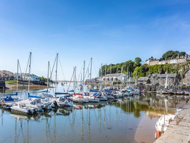A harbor with sailboats docked near stone buildings and houses on a hillside at Harbour View in Porthmadog