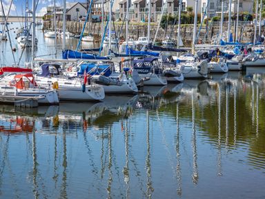 A harbor with multiple sailboats docked alongside a stone wall with houses in the background at Harbour View in Porthmadog