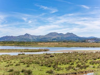 Wetland area with water channels and grass in front of a mountain range under a blue sky at Harbour View in Porthmadog
