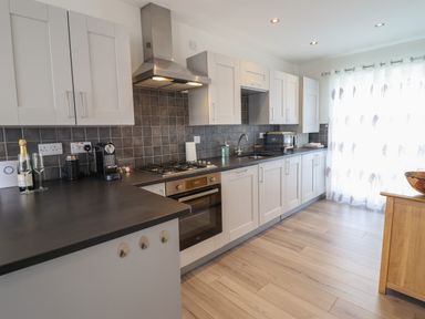 A kitchen with white cabinets countertop stove coffee maker and wooden floor at Harbour View in Porthmadog