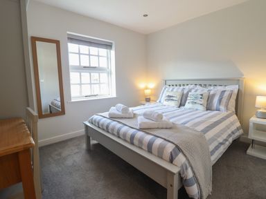 A bedroom with a double bed with striped bedding and rolled towels on top two nightstands with lamps a window with blinds and a wall mirror at Harbour View in Porthmadog