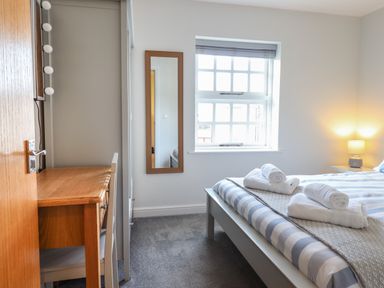 A bedroom with a bed with striped bedding and rolled towels near a window with blinds and a wooden desk with a chair and a mirror on the wall at Harbour View in Porthmadog