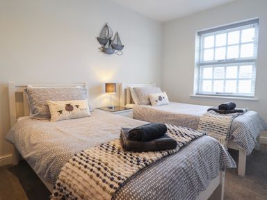 A bedroom with two single beds a nightstand with a lamp and a window at Harbour View in Porthmadog