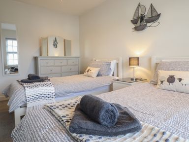 A bedroom with two single beds a dresser with a mirror a bedside table with a lamp and a wall decoration of boats at Harbour View in Porthmadog