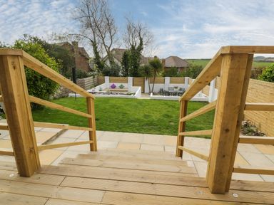 A backyard with wooden stairs and railings leading to a lawn paved area and garden seating at Estuary View in Newquay