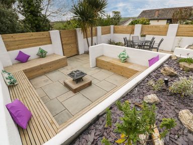 An outdoor seating area with wooden benches and colorful cushions around a fire pit and a dining table at Estuary View in Newquay