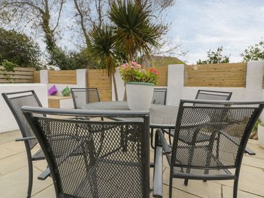 An outdoor patio with a metal table and six chairs a potted plant on the table and a seating area with cushions at Estuary View in Newquay