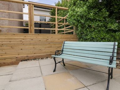 An outdoor area with a wooden bench on a paved surface next to a wooden fence and greenery at Estuary View in Newquay