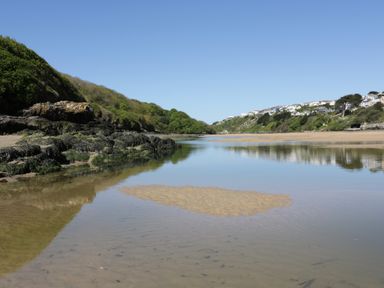 A river flowing between green hills with houses on the hillside at Estuary View in Newquay