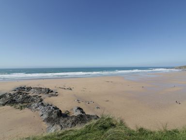 A beach with sand rocks some grass in the foreground and ocean waves at Estuary View in Newquay