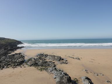 A sandy beach with rocks and ocean waves under a clear sky at Estuary View in Newquay