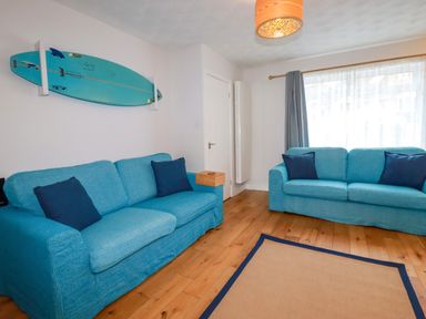 A living room with two blue sofas a surfboard mounted on the wall and a window with curtains at Estuary View in Newquay