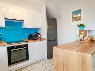 A kitchen with white cabinets a blue backsplash a black oven a microwave a silver refrigerator and a wooden countertop at Estuary View in Newquay