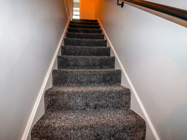 A stairway with dark carpet and white walls with a handrail at Estuary View in Newquay