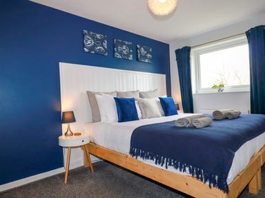 A bedroom with a wooden bed and blue and white bedding and pillows beside a small white nightstand with a lamp at Estuary View in Newquay
