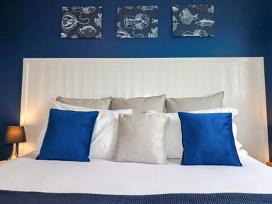 A bedroom with a white headboard blue and gray pillows and fish themed wall art at Estuary View in Newquay
