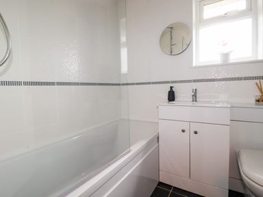 A bathroom with a bathtub a sink cabinet a round mirror and a window at Estuary View in Newquay