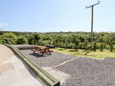 A picnic table on gravel with a grassy area and trees under a clear sky at The Lodge in Pontyates