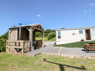 An outdoor wooden structure with a hot tub next to a mobile home with a bench outside at The Lodge in Pontyates