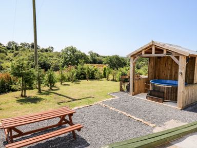 An outdoor area with a wooden picnic table and a covered wooden hot tub surrounded by grass and trees at The Lodge in Pontyates