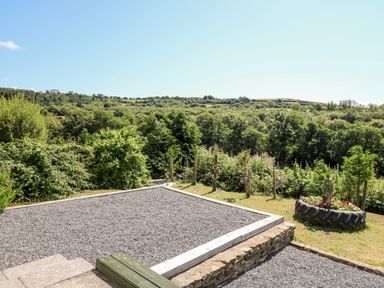 An outdoor gravel area bordered by wooden planks with surrounding greenery and a tire planter with flowers at The Lodge in Pontyates