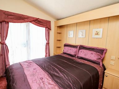 A bedroom with a double bed with purple and pink bedspread and pillows next to a window with pink curtains at The Lodge in Pontyates