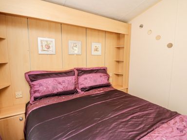 A bedroom with a bed with purple bedding and wooden shelves on the sides at The Lodge in Pontyates