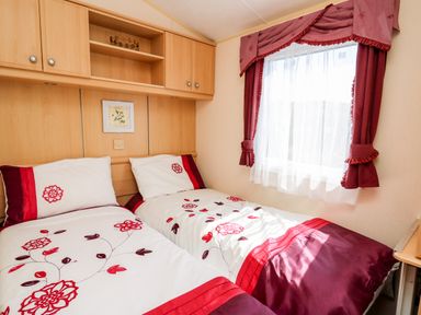A bedroom with two single beds with floral bedding and wooden cabinets above the beds at The Lodge in Pontyates
