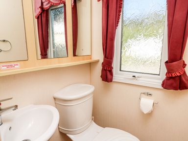 A bathroom with a toilet sink mirror and a window with red curtains at The Lodge in Pontyates