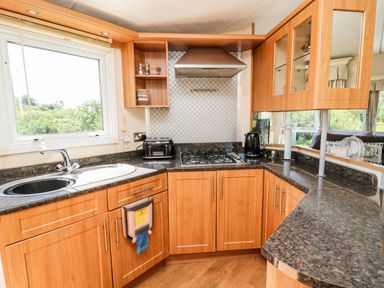 A kitchen with wooden cabinets black countertops a sink a gas stove toaster kettle and window at The Lodge in Pontyates