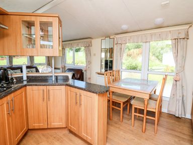 A kitchen with wooden cabinets and a dining area with a glass top table and four chairs at The Lodge in Pontyates