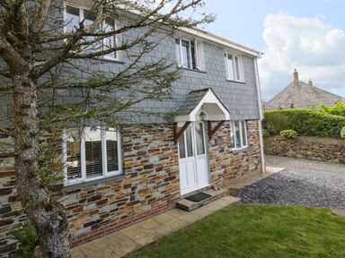 Exterior of a two story stone and gray shingle house with a white door and window at Hazel Cottage in Tintagel