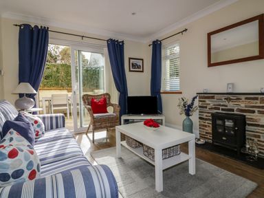 A living room with striped sofa or blue curtains and fireplace at Hazel Cottage in Tintagel