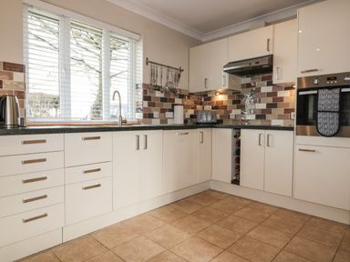 A kitchen with white cabinets a tiled floor a window with blinds and kitchen appliances at Hazel Cottage in Tintagel