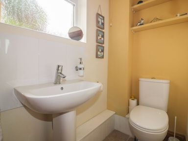 A bathroom with a white sink and a toilet with storage shelves above at Hazel Cottage in Tintagel