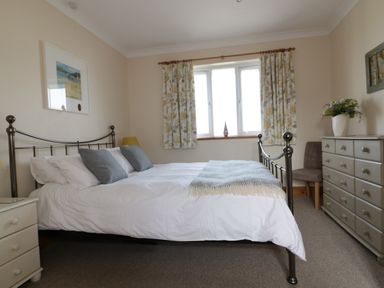 A bedroom with a metal bed frame white bedding and gray pillows a dresser with a plant and a chair at Hazel Cottage in Tintagel