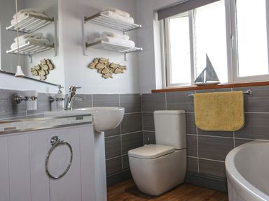 A bathroom with a toilet sink bathtub towel and shelves with towels at Hazel Cottage in Tintagel