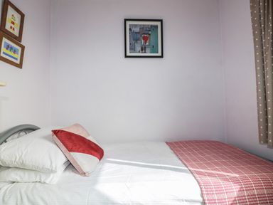 A bedroom with a bed with white sheets red and white striped pillow and red checkered blanket at Hazel Cottage in Tintagel