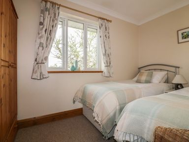 A bedroom with two single beds a wooden wardrobe and a window with curtains at Hazel Cottage in Tintagel