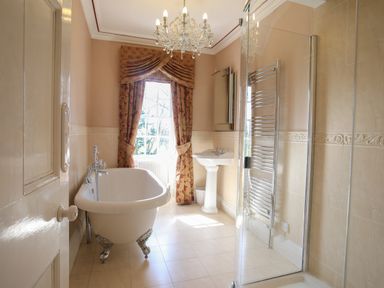 A bathroom with a clawfoot bathtub pedestal sink window with curtains and a glass shower at Tal Gwynedd in Dwyran near Newborough