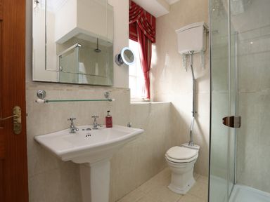 A bathroom with a sink a toilet with a high-level cistern a shower enclosure and a window with red curtains at Tal Gwynedd in Dwyran near Newborough