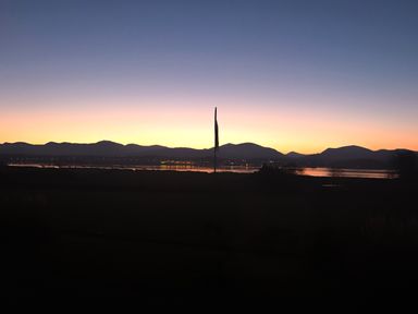 A sunset over a lake with mountains in the background and a flagpole in the center at Tal Gwynedd in Dwyran near Newborough