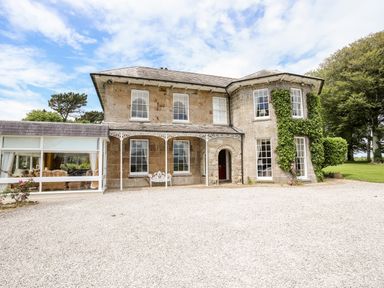 A stone house with multiple windows a gravel driveway and greenery climbing the walls at Tal Gwynedd in Dwyran near Newborough