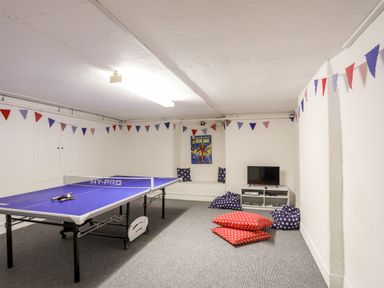 A game room with a ping pong table bean bags a small TV on a low white shelf and bunting on the walls at Tal Gwynedd in Dwyran near Newborough