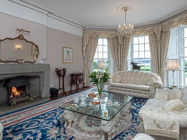A living room with a fireplace glass coffee table and floral carpet at Tal Gwynedd in Dwyran near Newborough