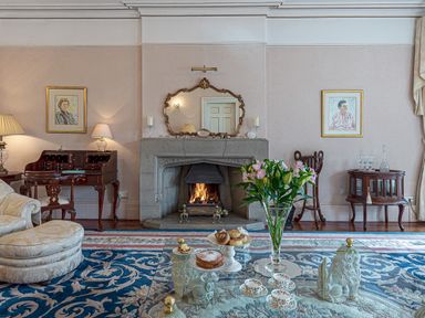 A sitting room with a fireplace flowers on a glass coffee table and paintings on the wall at Tal Gwynedd in Dwyran near Newborough