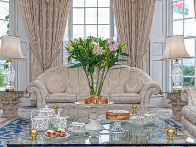 A sitting room with floral sofas a glass coffee table with flowers tea set and cakes at Tal Gwynedd in Dwyran near Newborough